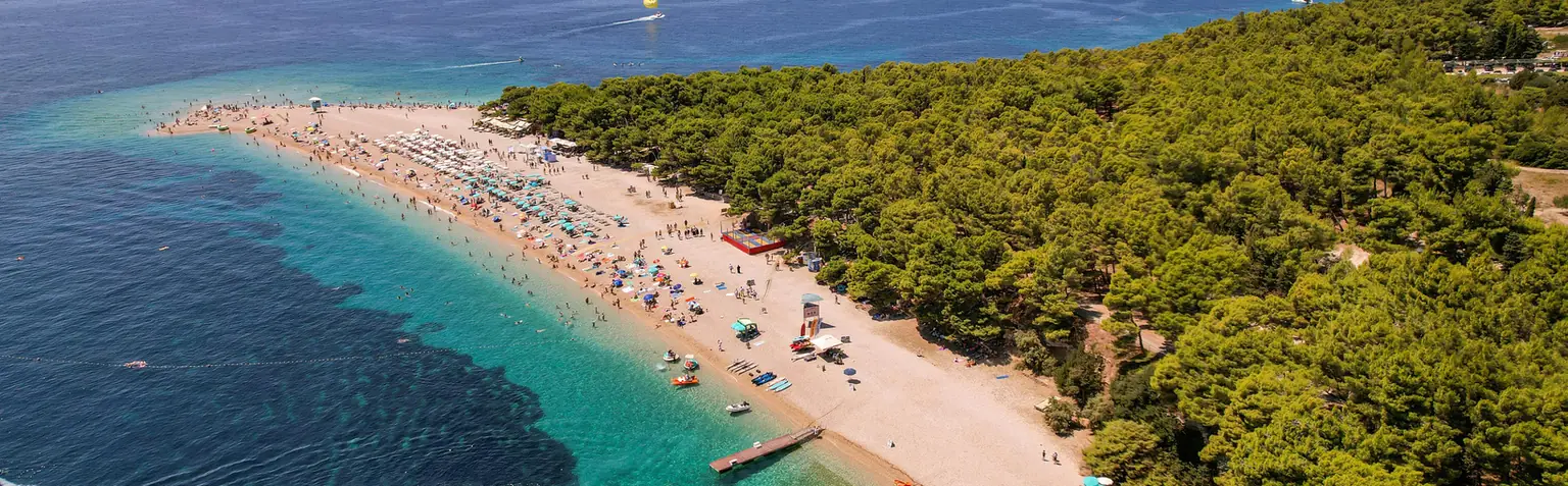 Zlatni rat s ležaljkama i suncobranima uz borovu šumu